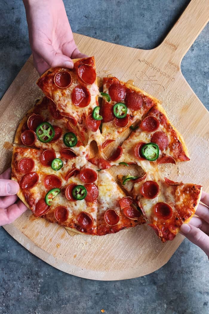 three hands pulling pieces of pizza off of a pizza peel