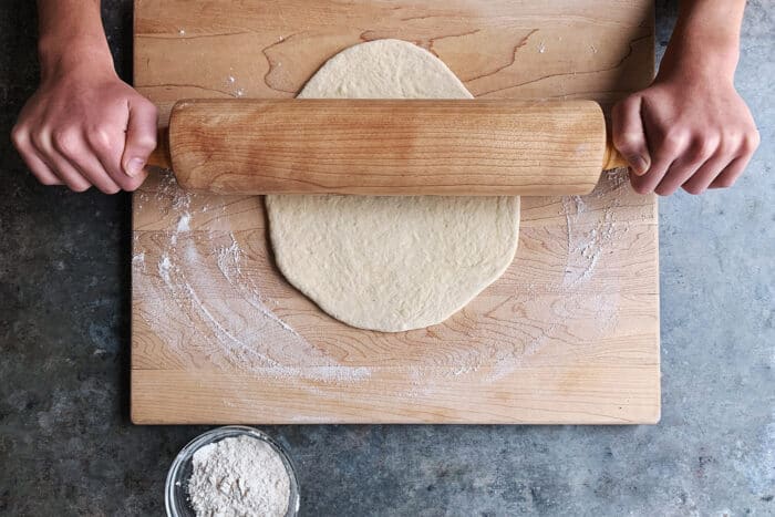 rolling out pizza dough on a wooden board