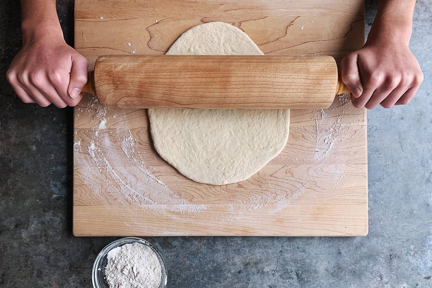 rolling out pizza dough on a wooden board