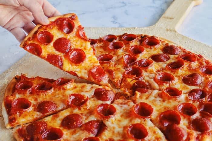 a hand taking a slice of pepperoni pizza