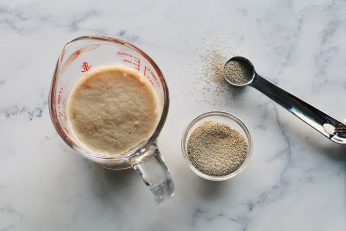 a small bowl of yeast, plus yeast foaming in a clear measuring cup of water