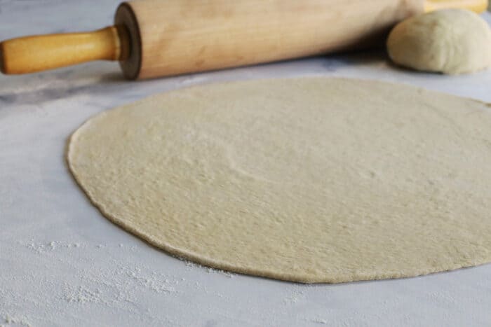 pizza dough rolled very thin on a white marble counter