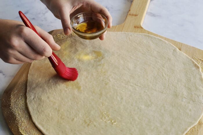 adding olive oil to the pizza dough crust with a kitchen brush