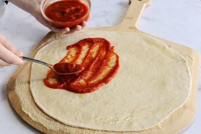adding pizza sauce to the pizza dough crust