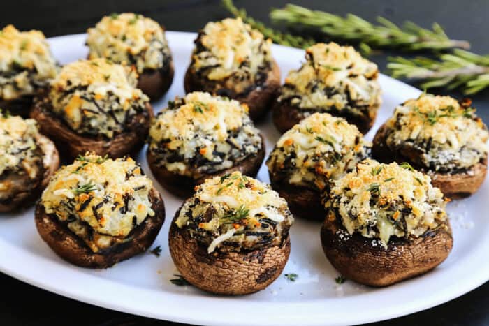 a white platter of baked stuffed mushrooms that are filled with mashed potatoes and wild rice