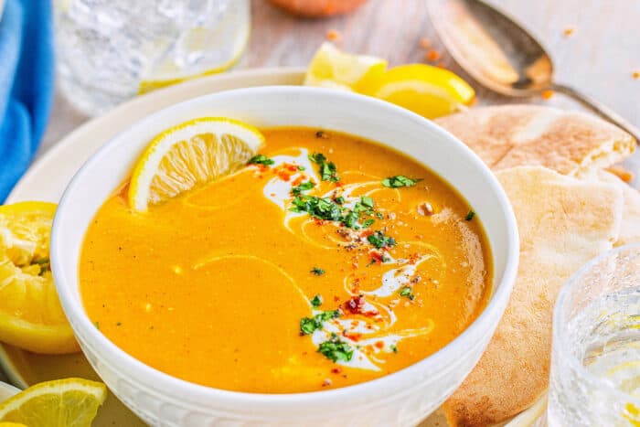 red lentil soup in a white bowl, with lemon slices and pita