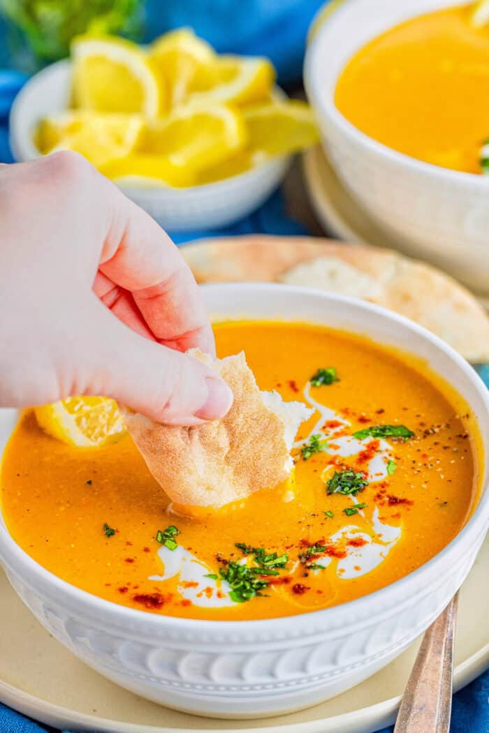 a hand dipping a torn piece of pita into bowl of soup