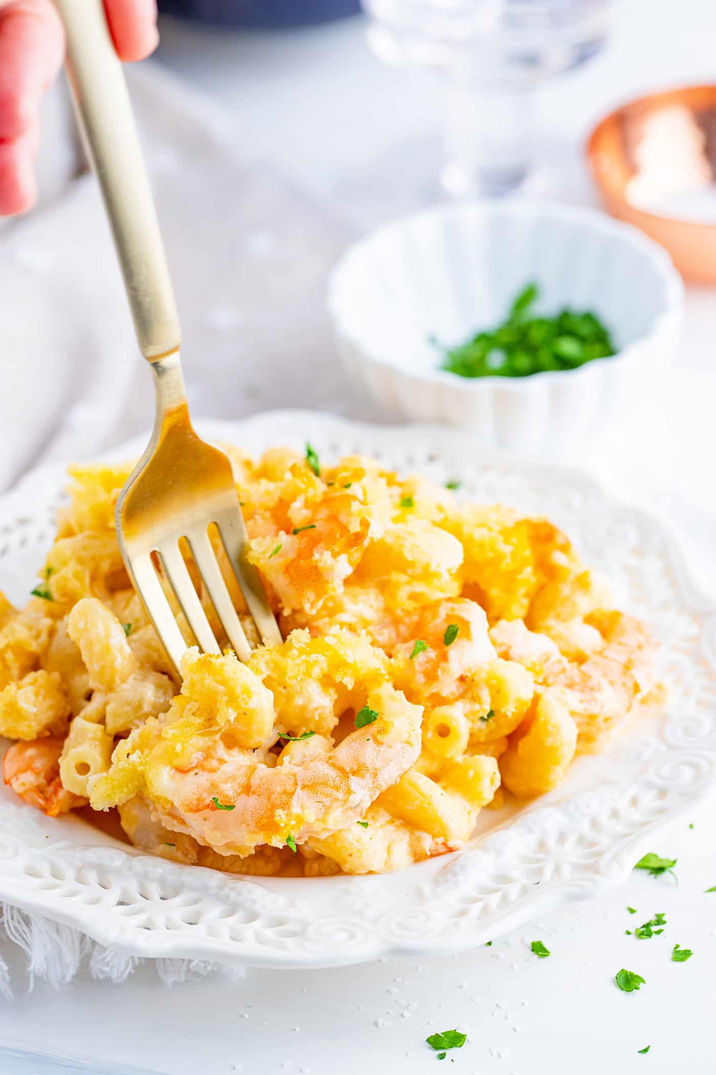 a fork digging into a plate of baked mac & cheese with shrimp