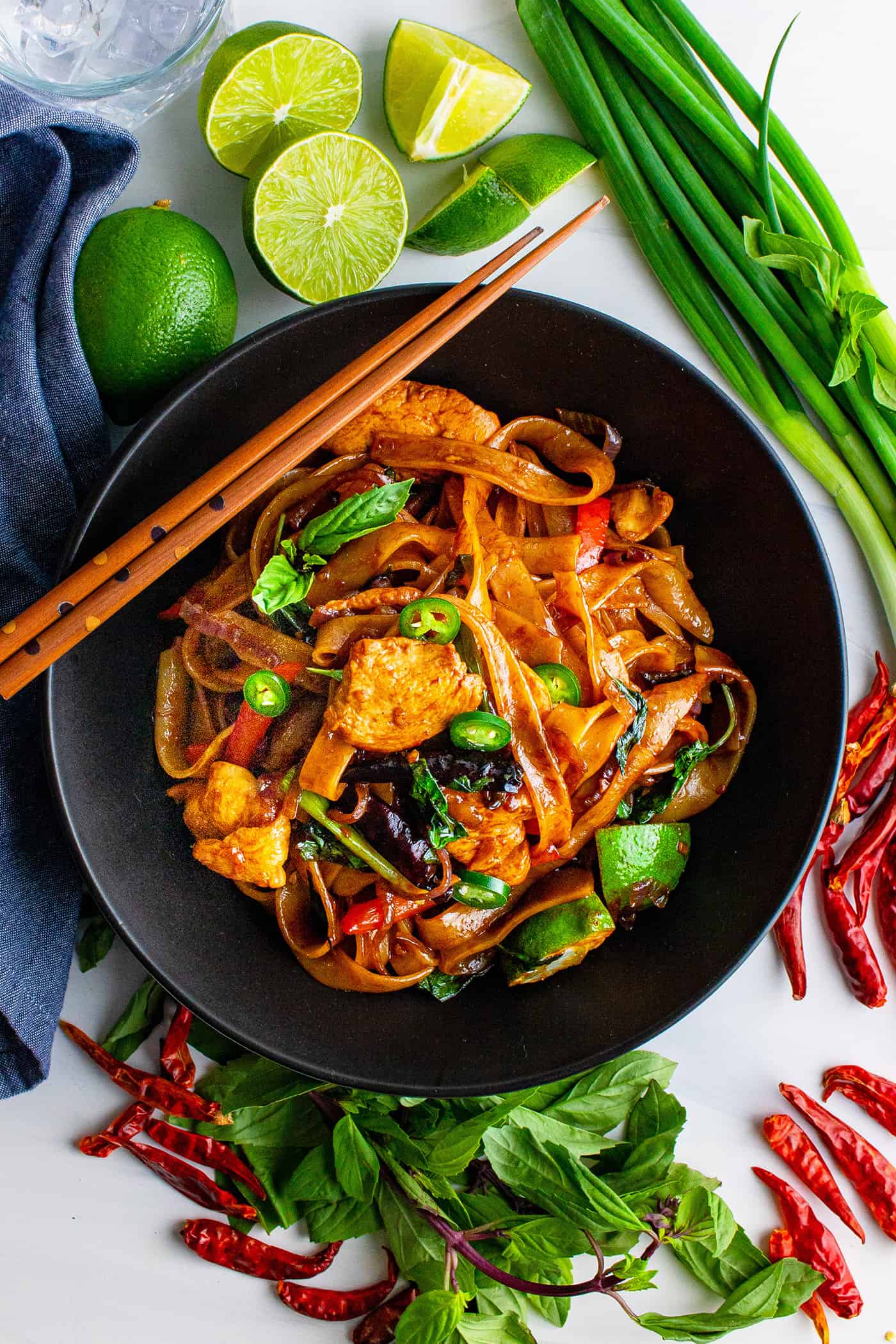 a black bowl of drunken noodles, with fresh ingredients on the table