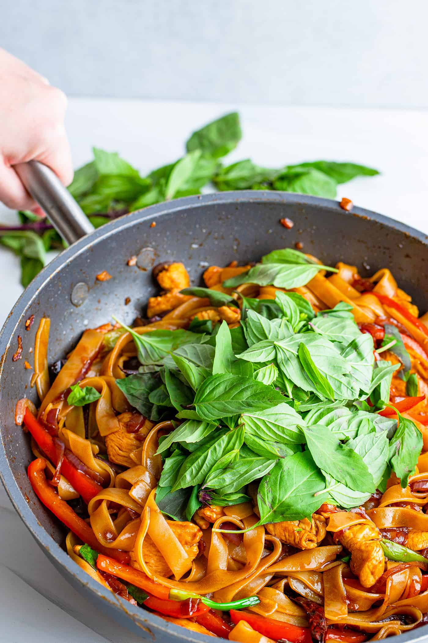 a pan of Thai drunken noodles topped with fresh Thai basil leaves