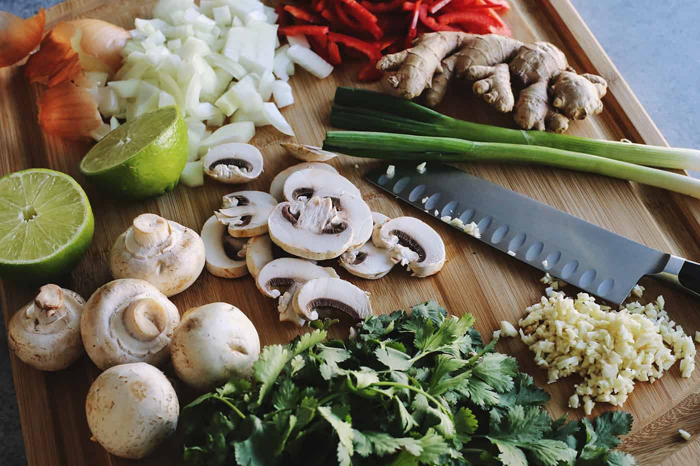 a wood chopping board and chef's knife, full of fresh vegetables being cut to add to the soup