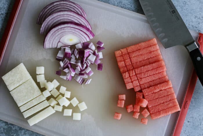 dicing watermelon, jicama, and red onion on a cutting board