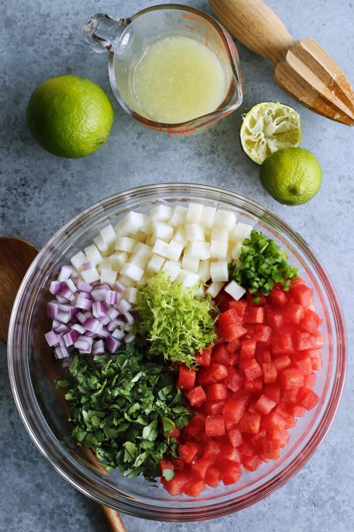 prepared ingredients for watermelon salsa in a clear bowl plus freshly squeezed lime juice