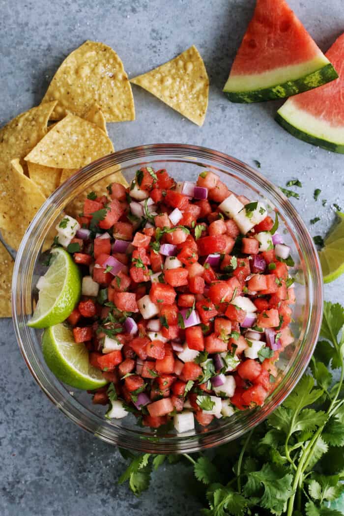 watermelon salsa in a clear bowl with tortilla chips and wedges of fresh watermelon