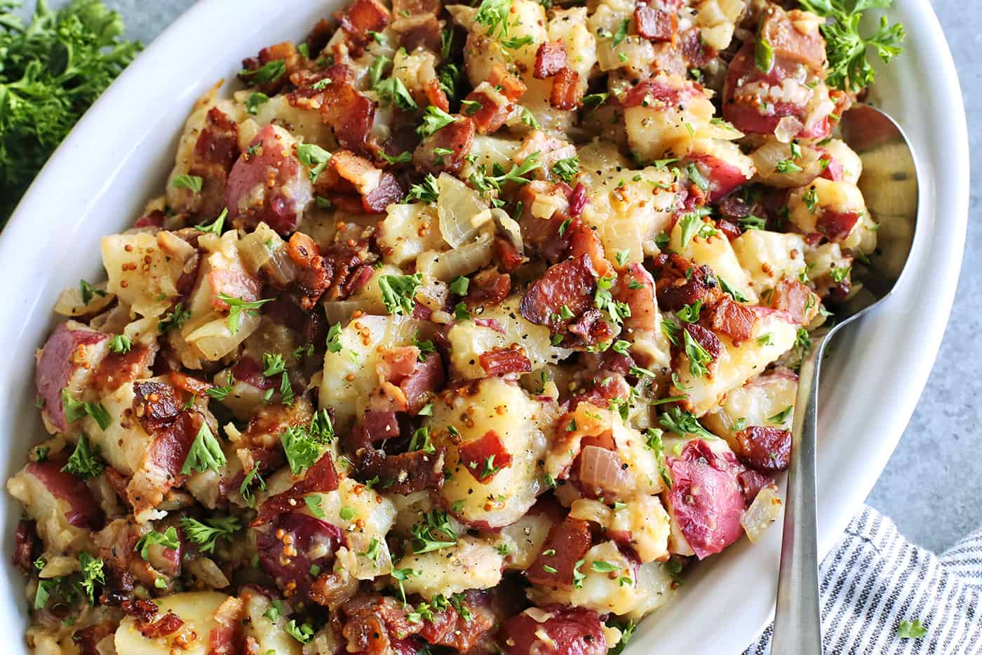 a large white platter with potato salad with pieces of bacon