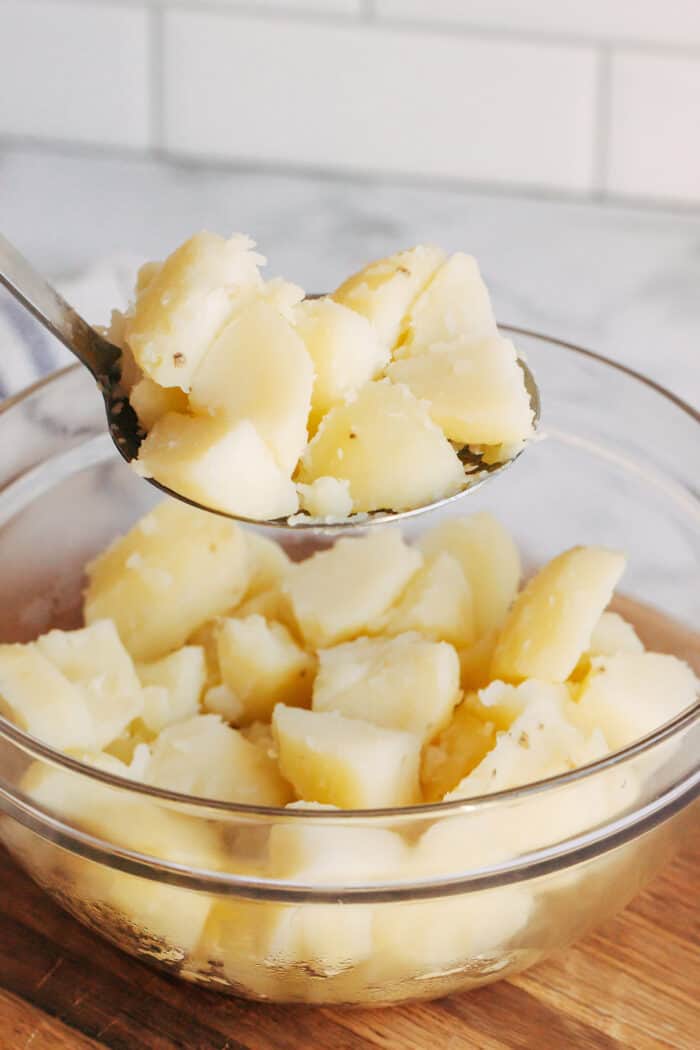 a big spoonful of cooked potato chunks, above a large clear bowl of cooked potato chunks
