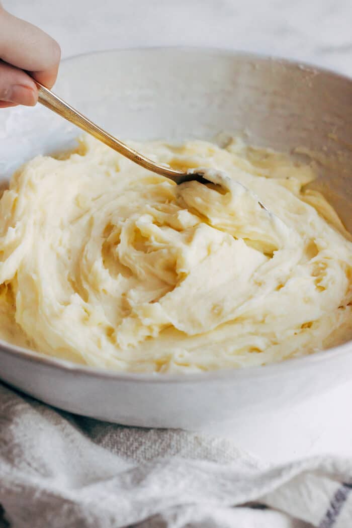 stirring creamy mashed potatoes in a large wide white bowl