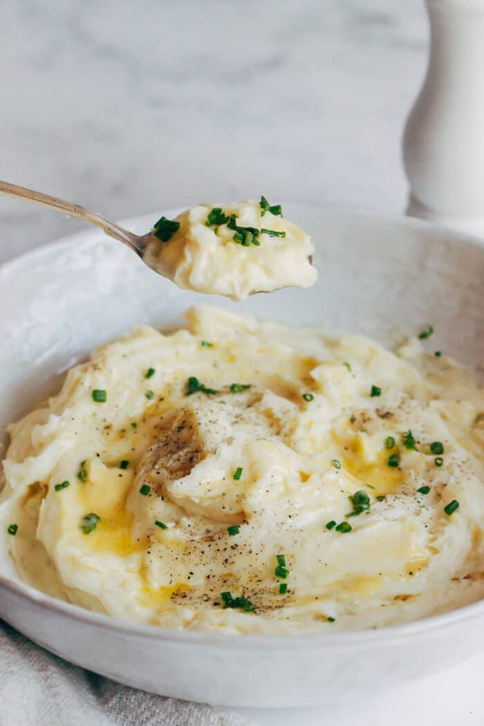 a spoonful of mashed potatoes being held above a bowl of the finished dish
