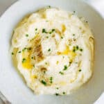 a white bowl full of mashed potatoes with butter and chives