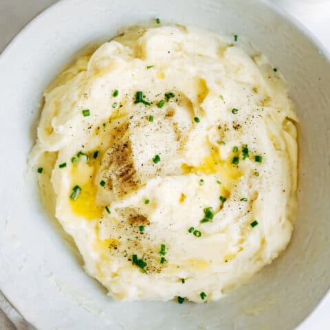 a white bowl full of mashed potatoes with butter and chives