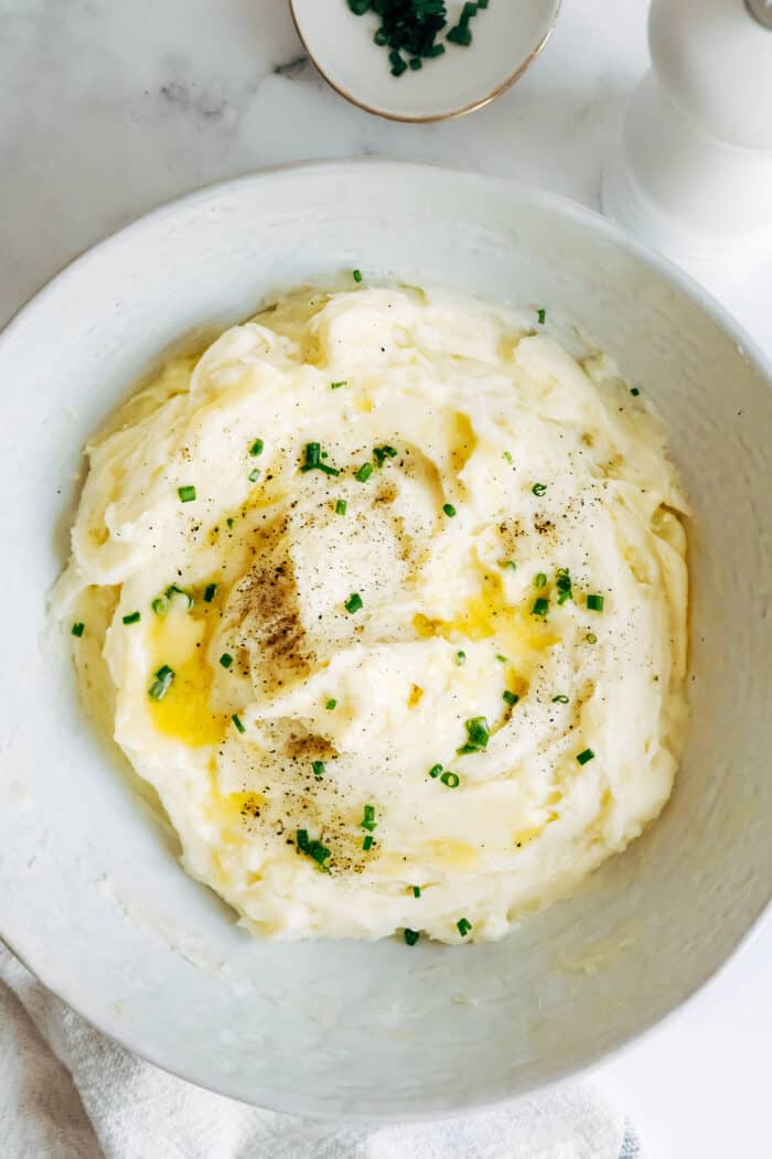 creamy mashed potatoes with melted butter and chives, in a large wide white bowl
