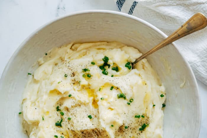 a spoon in a bowl of buttery mashed potatoes that are sprinkled with chives