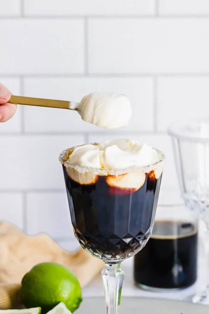 adding dollops of whipped cream to a coffee drink in a stemmed glass