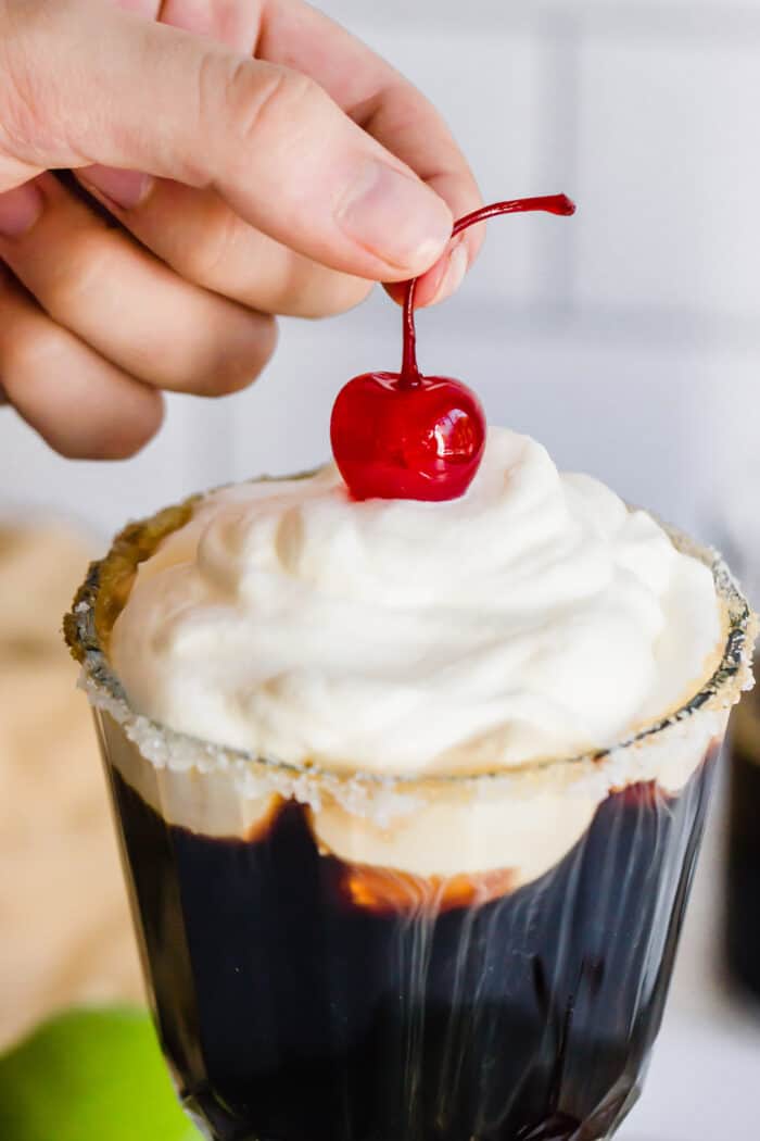 pressing a stemmed cherry into the whipped cream topping on a Mexican coffee