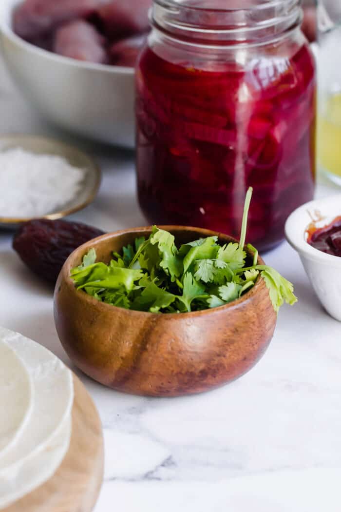 tortillas, cilantro in a small wood bowl, jar of pickled red onions