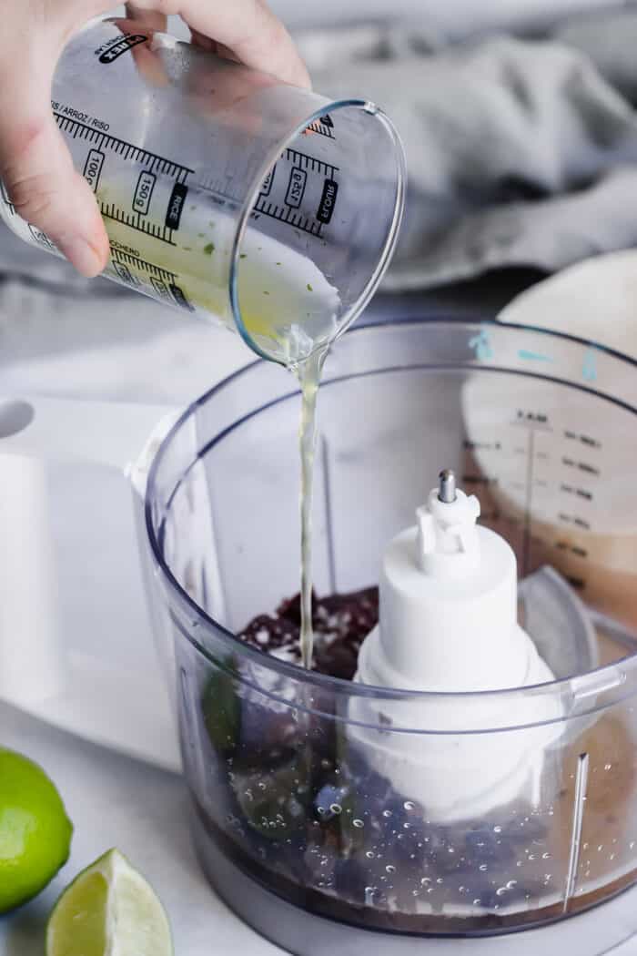 pouring chicken stock into a food processor to make the mole sauce