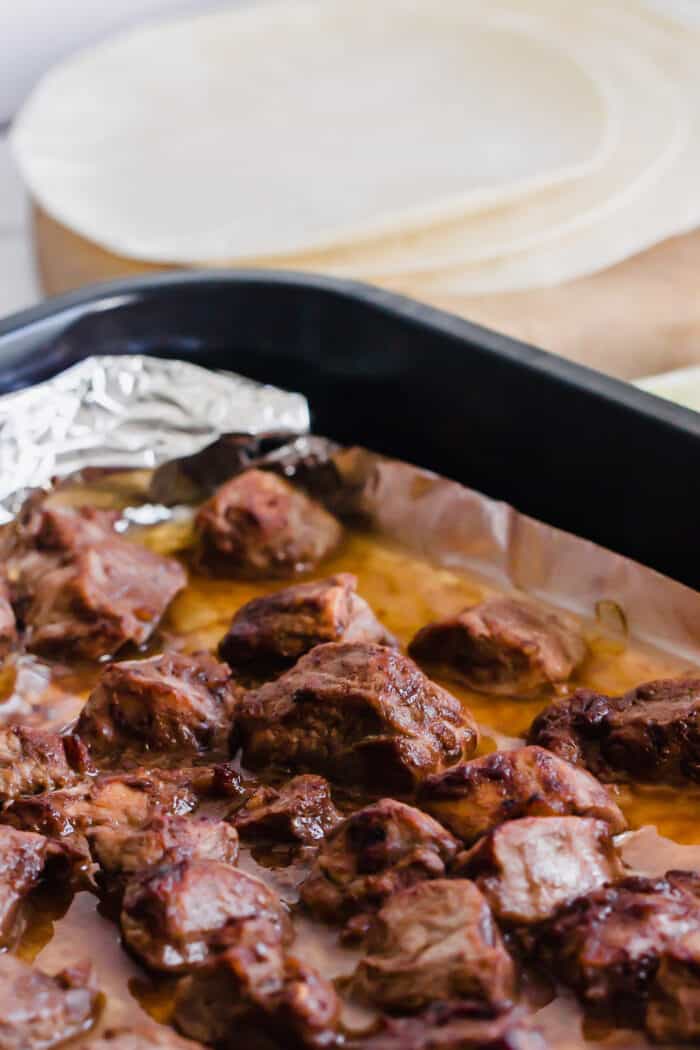 cubes of pork in a mole sauce marinade, cooked in a large metal baking pan