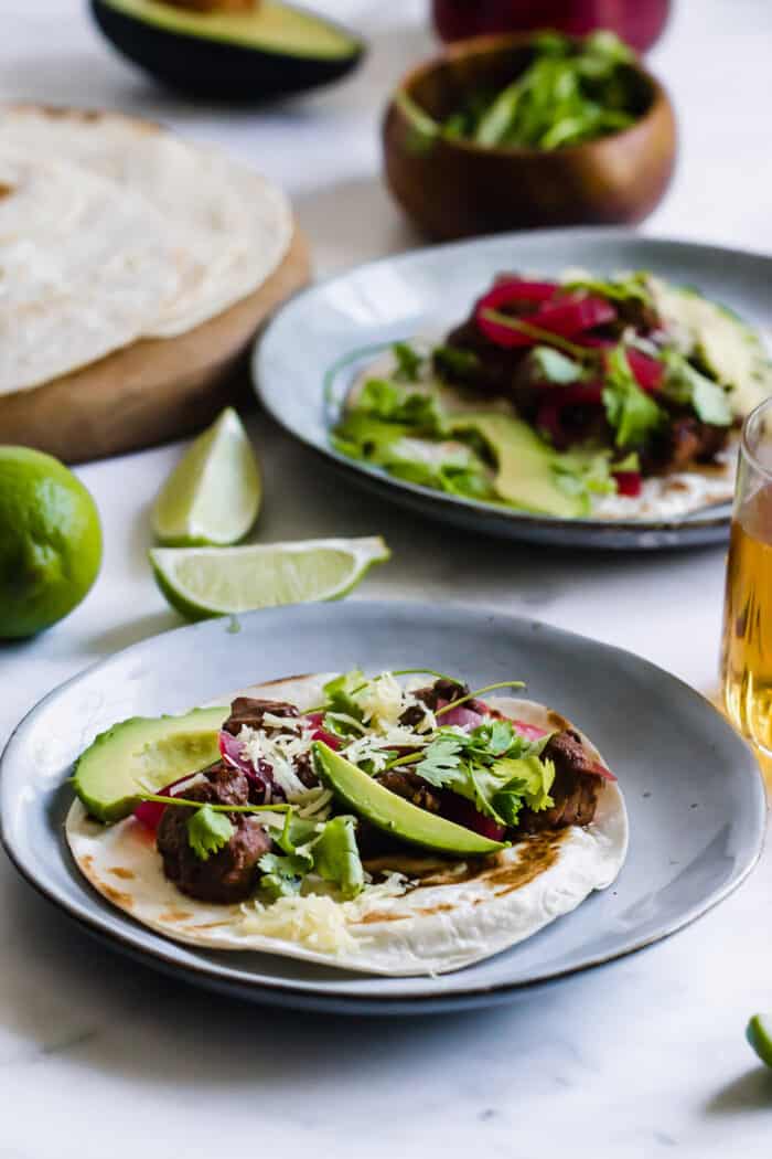 mole pork tacos on plates, plus fresh limes, tortillas, and a glass of beer