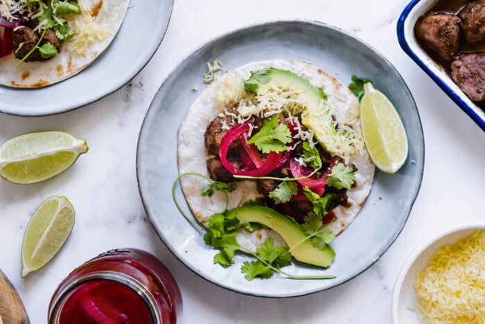 plates of pork tacos with mole sauce, a jar of pickled red onions, a pan of cooked mole pork