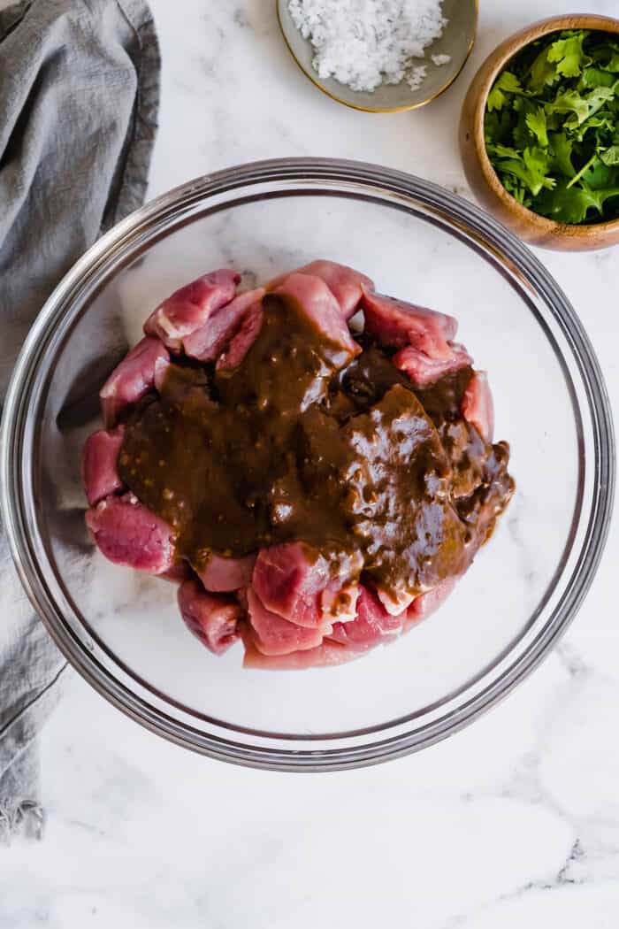 cubes of pork in a clear bowl with mole sauce poured over the top