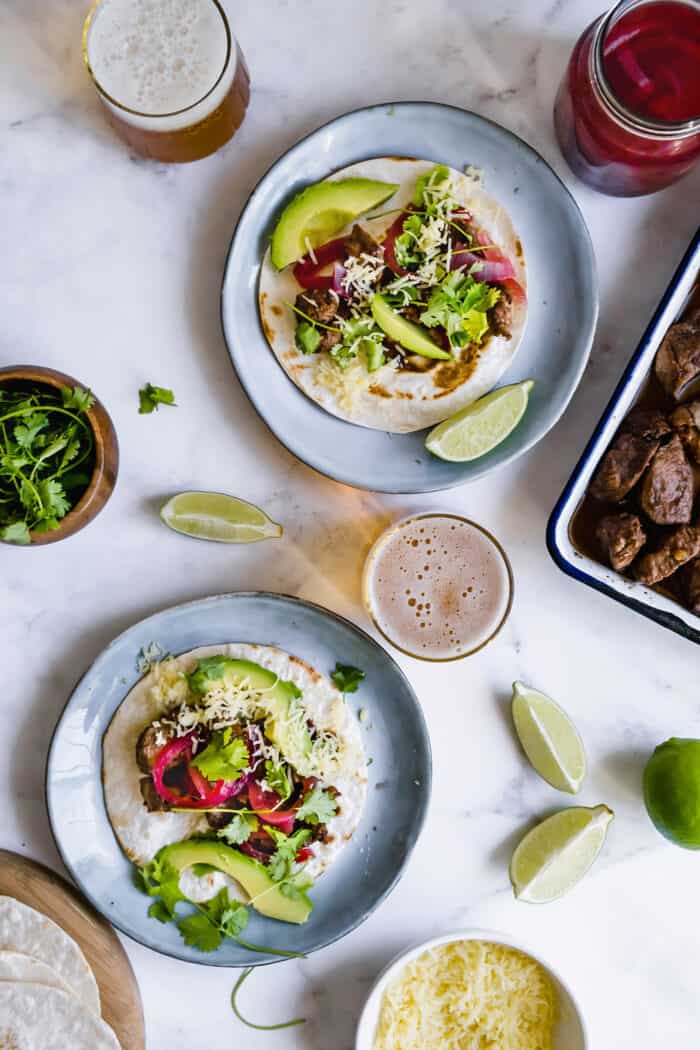 plates of tacos with pork mole, glasses of beer, a jar of pickled red onions, a pan of cooked pork