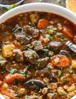 stew made of beef, barley, carrots, potatoes, and mushrooms, in a white bowl