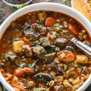 stew made of beef, barley, carrots, potatoes, and mushrooms, in a white bowl