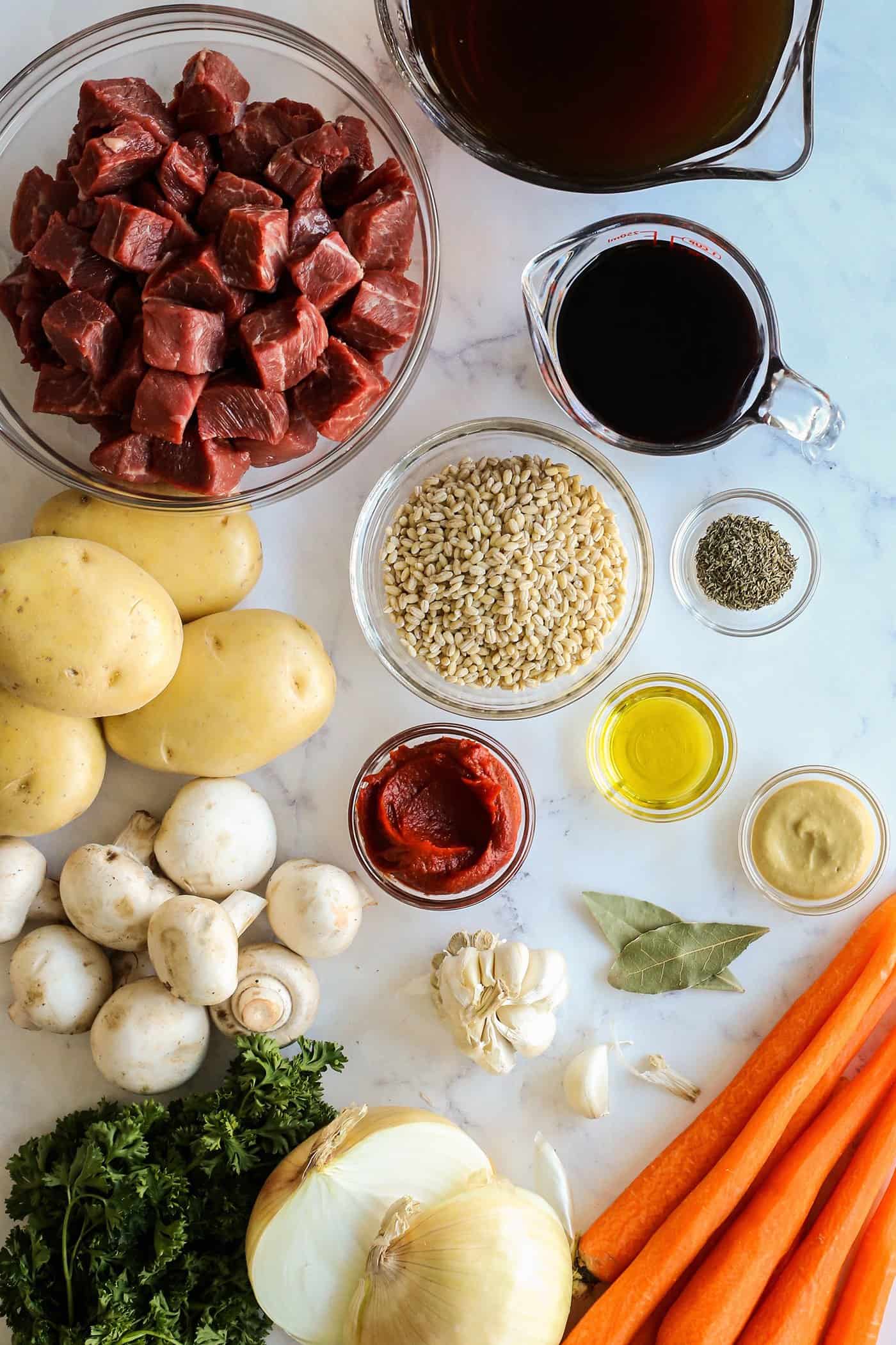 ingredients to make stew, to include cubes of beef, potatoes, barley, onion, mushrooms, carrots, beef stock, and red wine