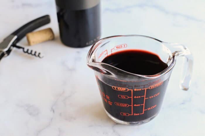 a glass measuring cup of red wine, plus a wine bottle and corkscrew in the background