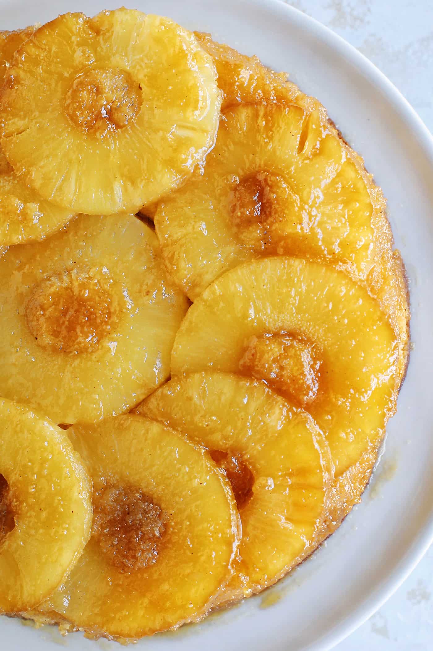This classic pineapple upside-down cake recipe has a rich, buttery cake with cozy spices and a caramelized brown sugar pineapple topping! Overhead view of a baked pineapple upside down cake topped with caramelized pineapples.