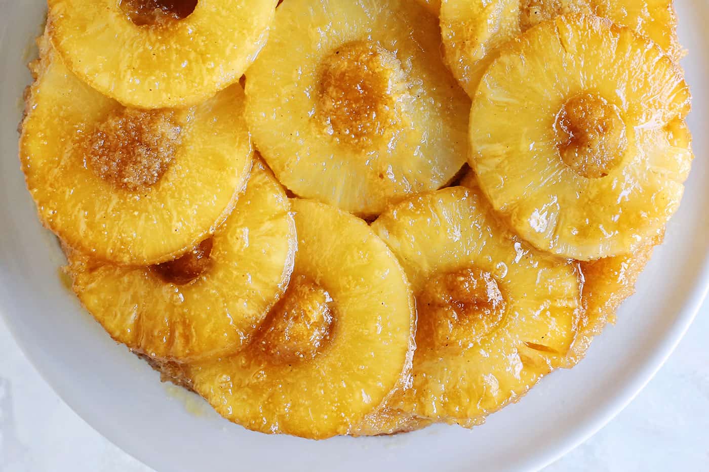 This classic pineapple upside-down cake recipe has a rich, buttery cake with cozy spices and a caramelized brown sugar pineapple topping! Overhead view of a baked pineapple upside down cake topped with caramelized pineapples.