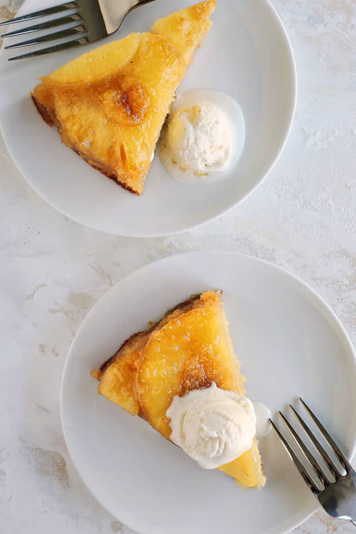 slices of pineapple cake with scoops of vanilla ice cream on white dessert plates