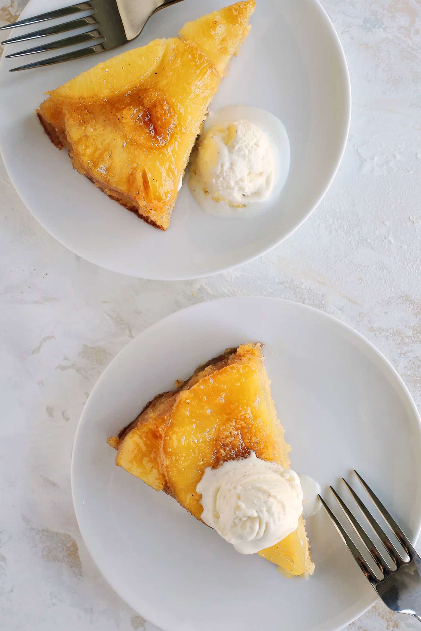 This classic pineapple upside-down cake recipe has a rich, buttery cake with cozy spices and a caramelized brown sugar pineapple topping! Overhead view of slices of pineapple upside-down cake with scoops of vanilla ice cream on small white plates.