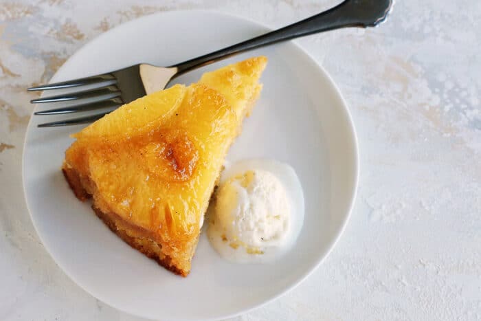 a slice of pineapple cake with a scoop of ice cream on a white plate