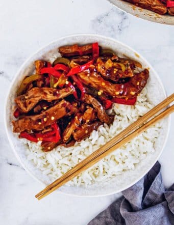 a white bowl with rice and Beijing beef, plus wooden chopsticks