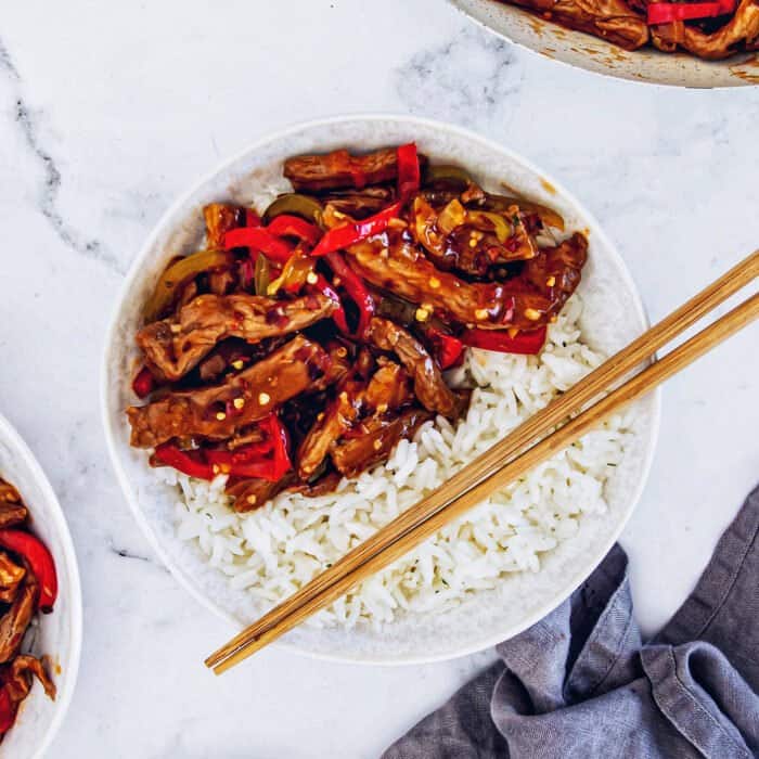 a white bowl with rice and Beijing beef, plus wooden chopsticks