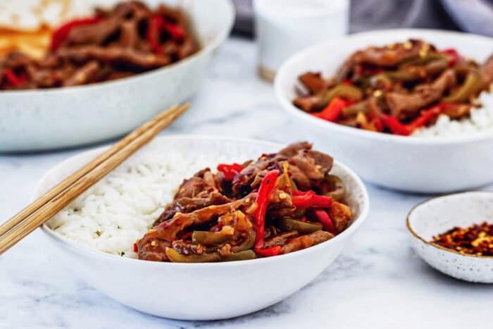 individual bowls of rice, beef, and vegetables with a skillet in the background