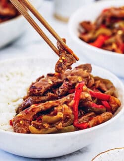 chopsticks holding a piece of Beijing beef over a white bowl