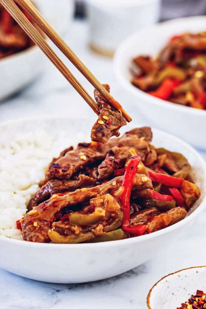 chopsticks holding a piece of Beijing beef over a white bowl