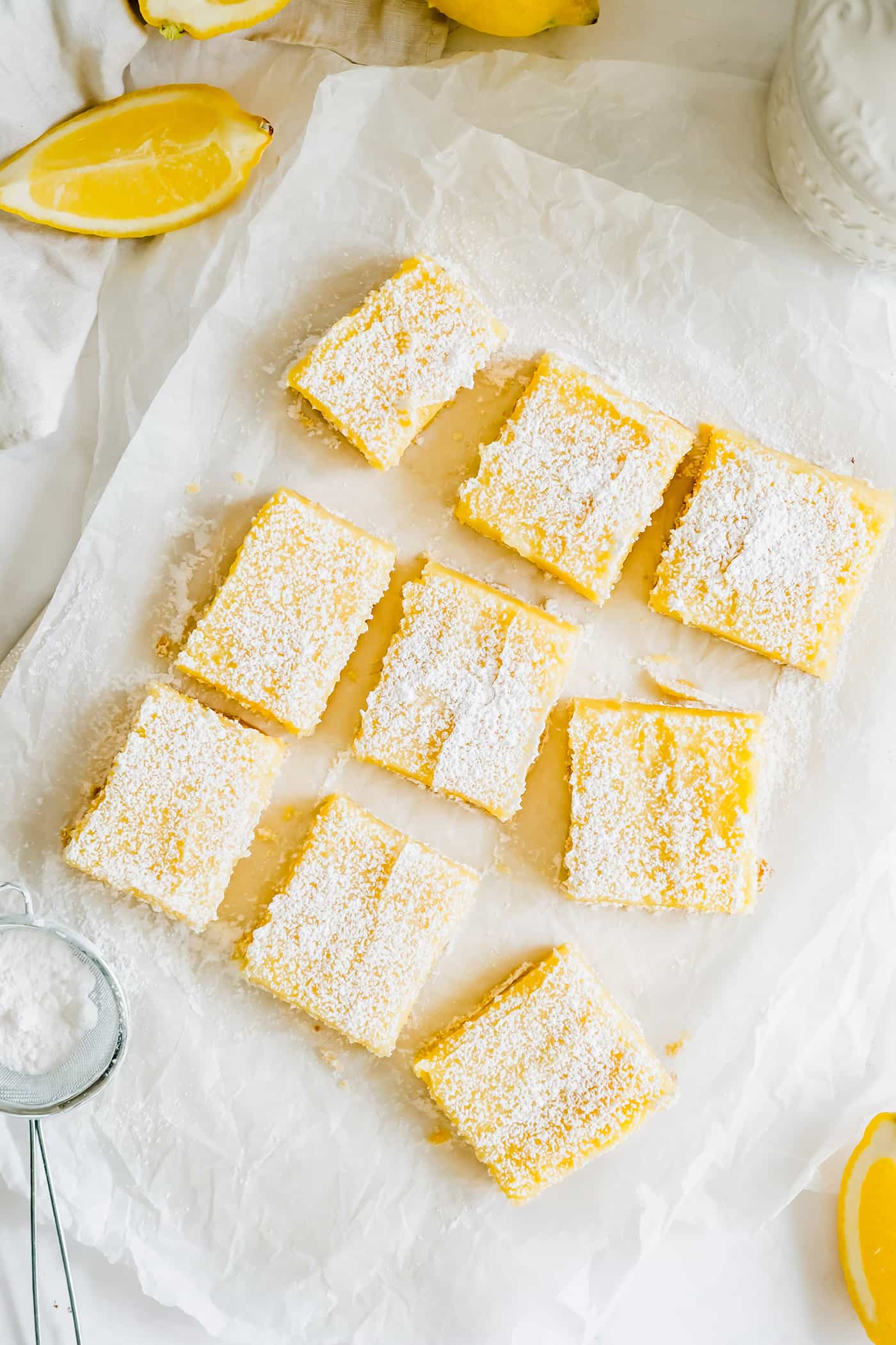 Lemon bars cut and sprinkled with powdered sugar, on a piece of white parchment paper